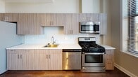 Located at 260 E Main St in the heart of downtown Rochester, NY, this modern residence offers a thoughtfully designed open layout with high-end finishes throughout. Rich, dark hardwood floors extend across the living areas, complementing the neutral tones of the walls and creating a warm, inviting atmosphere.

The kitchen is well-appointed with sleek light wood cabinetry, white quartz countertops, a glass tile backsplash, and a full suite of stainless steel appliances including a gas range, built-in microwave, and dishwasher. Large windows in the kitchen frame striking views of the Rochester skyline, including a picturesque clock tower landmark.

The open living area is bathed in natural light from a generous bank of windows, each fitted with adjustable blinds, offering expansive elevated views of the surrounding cityscape. Track lighting overhead adds functional versatility to the space.

The bedroom features the same beautiful hardwood flooring, ample closet storage with double doors, and additional room for flexible use. The bathroom is finished with large-format subway tiles in a classic white and tan pattern, a glass-enclosed walk-in shower, mosaic tile flooring, and a modern vanity with a framed mirror and contemporary fixtures. This residence combines urban convenience with refined, contemporary design.