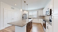 This single-story unit in Port Wentworth, Georgia, offers a thoughtfully designed layout that maximizes functionality across its comfortable footprint. The open-concept kitchen serves as the centerpiece of the home, showcasing crisp white shaker cabinetry, granite countertops, and a contrasting dark-base center island with pendant lighting overhead. Stainless steel appliances, including a French door refrigerator, dishwasher, microwave, and range, complete the well-equipped space. Wood-look luxury vinyl plank flooring runs throughout the main living areas, complementing the kitchen's clean aesthetic.

The living room receives generous natural light through a trio of windows dressed with blinds, and features a ceiling fan and the same warm wood-tone flooring. The bedroom is carpeted for comfort and includes direct outdoor access via a glass door, flanked by additional windows that bring in ample natural light and outdoor views. The bathroom features a glass-enclosed walk-in shower with tile surround and direct access to a dedicated closet with built-in shelving. Neutral tones and clean finishes throughout create a cohesive, move-in-ready atmosphere.