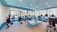 Located at 1588 Bloom St in Mount Pleasant, South Carolina, this modern fitness center is designed to support a comprehensive workout experience in a bright, welcoming environment. The single-floor facility is characterized by expansive floor-to-ceiling windows that line multiple walls, flooding the space with natural light and offering open views of the surrounding community.

The layout is thoughtfully organized into distinct workout zones. The cardio area is generously outfitted with a lineup of treadmills, elliptical machines, stationary bikes, and rowing equipment, all positioned to take advantage of the natural light and outdoor views. A wall-mounted television provides entertainment during workouts.

The strength training section features a variety of cable and resistance machines, along with a dedicated free weights area complete with a full dumbbell rack and adjustable weight bench. Full-length mirrors span an entire wall in this zone, enhancing the sense of space and allowing for proper form checks. Built-in open shelving runs below the mirrors, offering convenient storage.

The interior design reflects a coastal aesthetic, with a teal accent ceiling, white shiplap-style column details, and neutral-toned flooring throughout. Recessed lighting supplements the natural light, ensuring the space remains bright and energizing at any hour. A stretching table positioned centrally adds a functional recovery element to the facility.