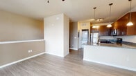 This well-appointed single-floor unit offers a thoughtfully designed open-concept layout that seamlessly connects the kitchen and living areas. The kitchen is a standout feature, showcasing rich dark-brown cabinetry, granite countertops with subtle speckled detailing, and a full suite of stainless steel appliances including a refrigerator, electric range, microwave, and dishwasher. A peninsula with an undermount sink and elegant pendant lighting serves as both a functional workspace and a natural divider between the kitchen and the living area. A wall-mounted mini-split system provides efficient climate control throughout the main living space, which is further complemented by a ceiling fan with integrated lighting. Light hardwood-style flooring extends throughout the unit, creating a clean, cohesive aesthetic. The living area benefits from natural light through windows and a sliding glass door that opens to an exterior entry, adding an airy, open feel to the space. A dedicated bathroom features a glass-door walk-in shower with built-in shelving and clean white surrounds. A staircase visible in the 3D model suggests access to shared building areas. Overall, the unit presents a modern, functional design with quality finishes throughout.