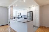 Located at 2 Kozlov St in Barrie, Ontario, this 2-bedroom, 1-bathroom unit offers a well-planned layout across a single floor. The open-concept living, dining, and kitchen area forms the heart of the home, bathed in natural light and unified by warm parquet flooring that extends throughout the main living spaces. The kitchen is a standout feature, outfitted with crisp white cabinetry reaching to the ceiling, stainless steel appliances including a refrigerator and electric range, recessed lighting, and a spacious peninsula with a stone-toned countertop — ideal for casual dining or meal prep. The living and dining area is generous in scale, with clean neutral walls and a hallway leading to the private quarters. The primary bedroom includes a sliding double closet, while the second bedroom features a window with views of the surrounding treed landscape and a baseboard heating unit. The full bathroom is finished with a white vanity, stone-toned countertop, large mirror, and a glass-enclosed shower/tub combination. A private balcony looks out onto a green, open outdoor setting with mature trees. White interior doors and textured ceilings complete the unit's tidy, functional aesthetic.