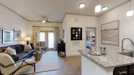 This single-floor residence offers a thoughtfully designed open-concept layout that seamlessly connects the kitchen, dining, and living areas. The kitchen features striking granite countertops and pendant lighting, with a breakfast bar that flows naturally into the main living space. Durable wood-look flooring extends throughout the common areas, adding warmth and continuity to the design.

The living room is bright and welcoming, highlighted by a ceiling fan, neutral-toned walls, and large glass doors that allow abundant natural light to fill the space while providing access to an outdoor area. Crown molding adds a refined architectural touch to the ceilings.

A glimpse into the bedroom reveals a well-lit, comfortable retreat with soft furnishings and ample space. The overall color palette throughout the residence is soft and neutral, creating a calm, cohesive ambiance that complements both the modern fixtures and the classic design elements.

The layout is practical and efficient, with clear sightlines from the kitchen through to the living area, making the space feel open and airy. Thoughtful details such as decorative lighting, coordinated window treatments, and quality finishes contribute to an overall atmosphere that is both functional and elegant.