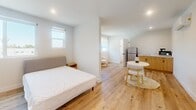 This thoughtfully designed one-bedroom, one-bathroom unit is located at 1165 West 37th Place in Los Angeles, CA. The single-floor layout makes efficient use of its space, featuring light wood flooring throughout that lends a warm, cohesive feel to the interior. Crisp white walls and recessed lighting create a bright, clean ambiance, while multiple windows allow natural light to filter in with views of the surrounding greenery.

The open living area flows seamlessly into a compact kitchenette equipped with wood-toned cabinetry, a stainless steel refrigerator, and a microwave. A wall-mounted mini-split unit provides climate control. A round dining table nestled in the main area offers a cozy spot for everyday meals.

The bedroom is generously proportioned relative to the overall footprint and features a wide window, built-in floor-to-ceiling white cabinetry for ample storage, and continued light wood flooring. A partially open layout connects it to the living space, enhancing the sense of openness.

The bathroom is a standout feature, showcasing large-format marble-look wall tiles and a walk-in shower with hexagonal mosaic floor tiles and matte black fixtures, delivering a polished, contemporary aesthetic throughout.