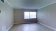 This single-floor space presents a clean and functional layout designed with a neutral, contemporary aesthetic. The interior is finished with light-toned ceramic or porcelain tile flooring throughout, offering a polished and easy-to-maintain surface that reflects natural light effectively.

The room showcases smooth, gray-painted walls paired with crisp white crown molding that adds a refined architectural detail along the ceiling perimeter. White baseboard trim further frames the space, providing a clean contrast against the neutral wall tones.

A prominent window positioned on the main wall is dressed with vertical blinds, allowing for flexible light control while permitting an ample amount of natural light to fill the room. The window contributes to the bright, open feel of the interior.

The ceiling features a subtle textured finish and is finished in white, enhancing the sense of height and spaciousness within the room. The overall ambiance is calm and understated, offering a versatile and move-in-ready environment that can accommodate a variety of uses. The minimalist design approach ensures the space feels open and adaptable to different furnishing styles and configurations.