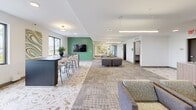 This contemporary office space, located at 5001 Palm Pointe Ct in Fort Myers, Florida, offers a well-designed 1600 square foot floor plan optimized for productivity and collaboration. The interior showcases a modern aesthetic with a harmonious blend of white walls and strategic green accent walls, creating a fresh and energizing atmosphere.

The space features an open-concept layout with multiple functional areas. A spacious central lounge area is furnished with comfortable grey sofas and armchairs, perfect for casual meetings or relaxation. Nearby, a kitchenette with high stools provides a convenient spot for quick breaks.

Several meeting rooms of various sizes are available, each equipped with sleek furniture and large windows that flood the spaces with natural light. These rooms offer views of the surrounding landscape, adding to the overall pleasant work environment.

The office boasts high-quality finishes throughout, including textured carpeting in neutral tones and suspended linear lighting fixtures. Thoughtful details such as artwork on the walls and potted plants contribute to a welcoming ambiance.

State-of-the-art technology is integrated seamlessly, with mounted displays in meeting rooms and common areas. The space also includes essential amenities like elevators and restrooms, ensuring comfort and accessibility for all occupants.

Overall, this office space combines functionality with modern design, creating an ideal setting for businesses seeking a professional and inspiring work environment.
