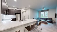Located in San Diego, CA 92115, this well-designed 3-bedroom, 3-bathroom unit offers a thoughtfully laid-out single-floor plan that maximizes functionality and comfort. The open-concept kitchen and living area serves as the heart of the home, featuring a large white quartz island with bar seating, dark espresso cabinetry, a full suite of stainless steel appliances — including a refrigerator, range, microwave, and dishwasher — and recessed lighting overhead. Light hardwood-style flooring flows throughout the main living areas, creating a clean, contemporary aesthetic. The living room is bright and inviting, highlighted by a large window that brings in natural light and outdoor views, a ceiling fan, and a wall-mounted TV. Each of the three bedrooms is carpeted and includes sliding closet doors, offering practical storage solutions. The primary bedroom provides a comfortable, private retreat. All three bathrooms are finished in a consistent modern style, featuring white subway tile tub-and-shower combos, clean white countertops, dark wood vanities, and large mirrors. A hallway connects the private and shared spaces efficiently. The overall ambiance is contemporary and clean, making this a well-appointed unit suited for shared or family living in San Diego.