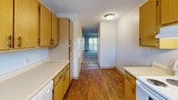 Located at 2726 S. Emporia St in Wichita, Kansas, this single-floor unit offers three bedrooms, two bathrooms, a kitchen, hallway, and closet within a compact and efficiently arranged floor plan. The kitchen is well-appointed with warm oak cabinetry, white countertops, a double-basin sink, a dishwasher, and ample upper and lower storage. Hardwood-style flooring runs through the kitchen and hallway, lending a clean, classic look, while a textured ceiling adds character throughout. The hallway connects the kitchen to the living and bedroom areas, with a vertical blind-covered window at the end allowing natural light to filter through. The spacious primary bedroom features plush carpeting, a dedicated closet, and direct access to a private bathroom. The en-suite bathroom includes a full tub-shower combination with white surround panels and oak overhead cabinetry. The two additional bedrooms are carpeted and each features a window for natural light and neighborhood views, with one room including a built-in closet with bifold doors. The second full bathroom mirrors the first with a tub-shower setup and oak cabinetry. The textured ceilings and neutral color palette are consistent throughout, creating a cohesive and functional living environment.