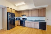 Located at 3445 Washington Blvd in Arlington, VA, this two-bedroom, two-bathroom residence offers a thoughtfully designed single-floor layout. Light hardwood flooring flows throughout the main living areas, complemented by crisp white walls and recessed lighting that create a clean, modern aesthetic. The open-concept living, dining, and kitchen area serves as the heart of the home, bathed in natural light from large, floor-to-ceiling windows that frame views of the surrounding Arlington cityscape. The kitchen is well-equipped with warm wood cabinetry extending to the ceiling for ample storage, dark countertops, and a full suite of black appliances including a gas range, refrigerator with ice maker, microwave, and dishwasher. A hallway with convenient louvered closet doors connects the main living space to the private quarters. Both bedrooms feature plush carpeting and bright white walls, with the second bedroom offering additional natural light through a large window. Three closets provide generous storage throughout. The two bathrooms are finished with neutral tile flooring; one features a full tub-shower combination with large-format tile surround and curved curtain rod, while the second offers a clean, minimalist design with a wood-toned vanity.