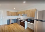This 620 square foot apartment offers a thoughtful layout maximizing space and functionality. The modern kitchen is a standout feature, boasting a sleek design with two-tone cabinetry - light wood upper cabinets and contrasting gray lower cabinets. Stainless steel appliances, including a dishwasher and range, complement the white subway tile backsplash and quartz countertops.

The spacious bathroom is notably accessible, with multiple grab bars and a wide doorway. It features a wooden vanity with ample storage, a large mirror, and a marbled-effect floor that adds a touch of sophistication.

The 170 square foot bedroom is generously sized for the apartment, with a large window allowing natural light to flood the space. Hardwood floors run throughout the living areas, bedroom, and kitchen, creating a cohesive and warm ambiance.

The living room, while compact, feels open and airy due to its connection with the kitchen and the presence of a window or sliding door, likely leading to a small outdoor space. A wall-mounted air conditioning unit provides climate control.

Overall, this single-floor apartment combines modern amenities with a practical layout, making efficient use of its 620 square feet to create a comfortable living space.