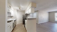 This single-floor residential unit offers a well-organized layout that balances functionality and comfort throughout its living spaces. The galley-style kitchen is outfitted with white cabinetry, stainless steel appliances including a refrigerator and range, a built-in dishwasher, and a sink with ample counter space. A peninsula with a light-toned countertop extends into the living area, creating a natural transition between the kitchen and main living space. Track lighting illuminates the kitchen, enhancing its clean, practical design.

The open living and dining area is a standout feature, showcasing stylish herringbone-patterned flooring that runs throughout the common areas, contributing to a cohesive and modern aesthetic. A large window in the living area allows natural light to fill the space, creating a bright and welcoming atmosphere.

The bedrooms are carpeted for comfort and feature neutral wall tones. One bedroom includes a sliding-door closet alongside built-in shelving and a built-in desk, providing convenient storage and workspace solutions. A ceiling fan adds to the room's functionality.

The bathroom is clean and efficiently designed, featuring a combined tub and shower unit with tile surround, a toilet, and a vanity with a light-toned countertop and a mirror. Herringbone flooring extends into the bathroom, maintaining visual continuity throughout the unit.