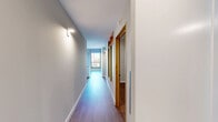 Located at 127 N 17th St in Richmond, VA, this one-bedroom, one-bathroom unit blends industrial character with modern finishes across a single, efficiently designed floor. The open living area makes a bold architectural statement with its exposed concrete ceiling and original textured accent walls, contrasted by warm hardwood flooring and large windows that frame views of the surrounding Richmond cityscape and flood the space with natural light. The kitchen is thoughtfully appointed with white shaker cabinetry, granite countertops, a classic subway tile backsplash, stainless steel appliances including a range with overhead hood, refrigerator, and dishwasher, plus a stainless undermount sink — a clean, functional layout well-suited for everyday cooking. A long hallway with wall sconces connects the main living area to the private bedroom and bathroom, lending a sense of separation and flow. The bedroom features sliding closet doors, hardwood flooring, and an exposed concrete ceiling that reinforces the industrial aesthetic. The bathroom offers a white vanity with granite countertop, a backlit LED mirror, tile flooring, and a barn-style door detail. An in-unit laundry area adds everyday convenience, completing this well-curated urban residence.