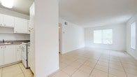This single-floor unit offers a clean, open layout designed for comfortable everyday living. The main living and dining areas are finished with large-format light-toned ceramic tile flooring, giving the space an airy and expansive feel. Multiple windows dressed with vertical blinds allow generous natural light to fill the rooms, enhancing the overall brightness of the white walls throughout.

A chandelier accent in the dining area adds a subtle decorative touch, while the open flow between the living, dining, and entry areas creates a seamless and functional layout. The kitchen features white cabinetry, speckled granite-style countertops, and a coil-burner range with overhead ventilation, providing a practical cooking space.

The bedrooms are distinguished by light wood-look plank flooring, offering a warm contrast to the tiled common areas. Each bedroom includes a louvered bifold closet door, providing dedicated storage. Textured ceilings are present in the bedroom areas, adding a classic finish detail.

Central air conditioning with ceiling vents is present throughout the unit, ensuring year-round climate control. The overall design is neutral and versatile, providing an ideal blank canvas that adapts easily to a variety of interior styles and furnishing preferences.