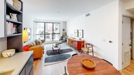 This thoughtfully designed single-floor residence blends contemporary style with functional living across a well-organized layout. The open-plan living and dining area serves as the heart of the home, featuring light oak hardwood flooring, crisp white walls, and expansive floor-to-ceiling windows that flood the space with natural light and offer dynamic urban views, including glimpses of palm trees and the surrounding cityscape.

The kitchen is outfitted with two-tone cabinetry — dark lower cabinets paired with white uppers — stainless steel appliances including a full-size refrigerator, range, and microwave, and a textured hexagonal tile backsplash. A dedicated entry area with direct access to the kitchen adds convenience.

The primary bedroom is a calm retreat with warm lighting, large windows, and access to a generous walk-in closet with built-in shelving and natural wood flooring. A versatile den or secondary bedroom features a built-in desk, wooden shelving unit, a sleeper sofa, and a window with street views — ideal as a home office or guest room.

Two well-appointed bathrooms each feature creamy hexagonal tile flooring and warm-toned subway tile walls. One includes a soaking tub with a curtain, while the other offers a glass-enclosed walk-in shower with a built-in niche. A stacked washer and dryer is conveniently located within the unit.