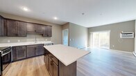 Located in Little Falls, MN, this well-designed 2-bedroom, 2-bathroom single-floor unit offers a functional and modern living experience. The open-concept kitchen and living area serves as the heart of the space, where light hardwood flooring flows throughout. The kitchen is outfitted with rich dark-stained cabinetry, stainless steel appliances including a refrigerator, range, and microwave, and a central island topped with a crisp white countertop — ideal for both meal preparation and casual dining. The adjacent living room is bathed in natural light from large sliding glass doors that open onto a private balcony overlooking a lush, tree-lined outdoor setting. Both bedrooms are carpeted and well-lit, with the second bedroom featuring a large window framing tranquil views of the surrounding greenery. The primary bedroom is a comfortable size with its own dedicated closet. Two full bathrooms are finished with dark wood vanities, white countertops, and hardwood-style flooring, maintaining a consistent and clean aesthetic. Two closets provide ample storage throughout the unit. Neutral warm-toned walls, recessed lighting, and baseboard heating complete the thoughtfully appointed interior of this Little Falls residence.