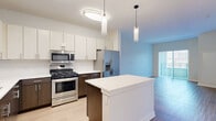 Located at 400 N Main St in Glen Ellyn, IL, this thoughtfully designed one-bedroom, two-bathroom residence offers a efficient and modern single-floor layout. The open-concept kitchen and living area serves as the heart of the home, featuring a sleek kitchen with two-tone cabinetry — white upper cabinets paired with rich dark wood lower cabinets — complemented by clean white quartz countertops, a central island, and a full suite of stainless steel appliances including a gas range, built-in microwave, and French door refrigerator. Pendant lighting and light wood-tone flooring add warmth and contemporary style to the space. The living area flows naturally from the kitchen and opens to a balcony through sliding glass doors with vertical blinds, allowing abundant natural light. The carpeted bedroom offers a comfortable retreat with a large window overlooking the neighborhood. A spacious walk-in closet with wire shelving provides generous storage. The bathrooms are finished with elegant stone-look tile surrounds and clean white fixtures. Throughout the residence, a neutral color palette and modern finishes create a bright, cohesive, and inviting atmosphere.