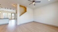 This two-story residence offers a well-organized layout across two floors, with the main living areas on the ground floor and bedrooms above. The ground floor centers around an open-concept kitchen and living room, finished with light wood-style flooring that extends throughout. The kitchen is appointed with dark espresso cabinetry, granite countertops, a subway tile backsplash, stainless steel appliances, a peninsula island, and pendant lighting complemented by a track lighting system. Large windows and a glazed door at the rear of the living area allow substantial natural light to fill the space. A ceiling fan with integrated lighting serves the living room, and a staircase with a warm-toned wood finish connects to the upper floor.

The upper level houses all three bedrooms, each carpeted and equipped with large windows that provide outdoor views and ample natural light. The generously sized primary bedroom includes a dedicated walk-in closet with wire shelving on multiple walls. A second walk-in closet offers additional storage with comparable shelving. Two full bathrooms serve the home, one featuring a soaking tub with white subway tile surround. The overall aesthetic is clean and contemporary, with neutral tones maintained throughout both floors.