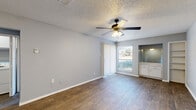 This single-floor residence offers a thoughtfully arranged layout encompassing a living room, kitchen, bedroom, bathroom, and closet. The living area is finished with warm wood-look flooring, neutral gray walls, and a textured ceiling, with a ceiling fan providing both light and airflow. Natural light enters through a window fitted with vertical blinds, and a built-in cabinet nook adds a functional accent. The kitchen is efficiently designed in a galley style, featuring white cabinetry, white countertops, a gray tile backsplash, a stainless steel sink, and black and stainless steel appliances including an electric range, dishwasher, and over-the-range microwave. A dedicated laundry closet with side-by-side washer and dryer units is conveniently located off the main living area. The bedroom is carpeted for comfort, featuring a window with natural light and ample wall space. The full bathroom includes a single-sink vanity with white cabinetry, a combined shower and bathtub with white tile surround, and wood-look tile flooring. Throughout the residence, a consistent gray and white color palette creates a clean, cohesive aesthetic.