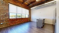 Located at 1100 N 2nd Street in Leavenworth, Kansas, this one-bedroom, one-bathroom loft blends industrial character with contemporary upgrades. The open living and kitchen area immediately impresses with soaring ceilings adorned with exposed wooden beams and visible ductwork, alongside a striking exposed brick accent wall that adds warmth and historic charm. Large windows with roller shades flood the space with natural light while offering views of the surrounding greenery, complementing the durable wood-look flooring found throughout. The kitchen is a functional highlight, featuring a peninsula with a granite countertop and integrated sink, gray shaker-style cabinetry, a subway tile backsplash, and stainless steel appliances including a refrigerator, electric range, dishwasher, and built-in microwave. The galley-style layout provides ample counter and storage space. The bedroom is a comfortable, well-proportioned retreat with neutral carpet flooring, clean white walls, and a dedicated closet for storage. The bathroom is finished with consistent gray cabinetry topped with granite, wood-look flooring, and a full tub-shower combination. This thoughtfully designed loft offers an efficient and stylish living environment with a distinctive industrial-urban aesthetic.