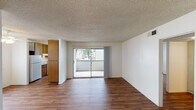 This single-floor residence offers a clean, functional layout designed for comfortable everyday living. The open living area is finished with warm wood-look hardwood-style flooring that runs throughout the main living spaces, complemented by crisp white walls and a textured popcorn ceiling. A ceiling fan adds both style and practicality to the living area, which is bathed in natural light from a large sliding glass door that opens directly onto a private balcony, providing pleasant outdoor views.

The kitchen is conveniently positioned adjacent to the living area and features warm wood cabinetry, a white refrigerator, an electric range, and ample counter space — making it well-suited for everyday meal preparation.

The bedroom offers a change in flooring with soft, neutral-toned carpet underfoot, creating a cozy and restful atmosphere. A large window with vertical blinds allows natural light to fill the room, while a closet provides dedicated storage space.

The bathroom is outfitted with a full-size tub and shower combo, surrounded by clean white tile, offering a straightforward and functional design. A hallway connects the bedroom and bathroom seamlessly to the rest of the unit.

Overall, the space presents a practical and well-organized floor plan with consistent finishes, abundant natural light, and outdoor access that enhance daily living.
