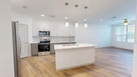 Located at 5750 Airport Rd in Santa Fe, NM, this well-appointed one-bedroom, one-bathroom unit offers a thoughtfully designed single-floor layout with modern finishes throughout. The open-concept kitchen and living area serves as the heart of the space, anchored by a large central island with a built-in sink and pendant lighting above. The kitchen features two-toned cabinetry — white upper cabinets paired with gray lower cabinets — complemented by a marble-style tile backsplash, stainless steel appliances, and light wood-tone flooring that extends seamlessly into the living area. The bedroom is a comfortable, carpeted retreat with a ceiling fan, large windows that invite natural light, and a private door providing outdoor access. A dedicated walk-in closet offers built-in shelving and hanging rods for ample storage. The full bathroom is clean and contemporary, featuring gray shaker-style cabinetry, a white countertop vanity with a large mirror, and a tiled walk-in shower. Recessed lighting throughout the main living areas enhances the bright, airy ambiance. The overall aesthetic is fresh and modern, with a neutral palette that creates a welcoming and versatile living environment.