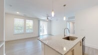 This single-floor residence features a clean, contemporary design characterized by an all-white color palette, light wood-style flooring, and abundant natural light throughout. The open-concept kitchen serves as a central hub, outfitted with white shaker-style cabinetry, granite countertops, a subway tile backsplash, and black Whirlpool appliances including a refrigerator, range, and over-the-range microwave. A spacious island with an undermount sink anchors the kitchen and flows seamlessly into the living area, which is illuminated by pendant lighting and a ceiling fan. Sliding glass doors open to a balcony, while multiple windows frame views of surrounding greenery. A hallway connects the private quarters, including generously sized bedrooms, each with ceiling fans and ample natural light. The bathrooms are well-appointed, featuring granite-topped vanities, white cabinetry, and both a glass-enclosed walk-in shower and a separate soaking tub with white tile surround. The hallway includes recessed lighting and a smart thermostat, adding a functional, modern touch to this bright and cohesive living space.