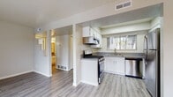 This single-floor residence offers a clean, modern aesthetic with light wood-look flooring that flows seamlessly throughout every room, creating a cohesive and inviting atmosphere. The kitchen is well-appointed with white shaker-style cabinetry, granite-look countertops, stainless steel appliances including a gas range with overhead microwave, and a dishwasher. A window above the sink allows natural light to brighten the workspace. The open layout connects the kitchen to the rest of the living areas, enhancing the sense of space and ease of movement. The living room is a standout area, featuring a fireplace as a central focal point, a sliding glass door that opens to an outdoor space, a window with window AC unit, and ample room for comfortable furnishings. A ceiling fan adds to the functionality of the space. The bedrooms are well-sized, each with windows that invite natural light, and one features a wall-mounted light fixture at the entry. The full bathroom is neatly finished with a white vanity, granite-look countertop, brushed nickel hardware, a large mirror, and a full tub-shower combination. Throughout the residence, neutral wall tones and consistent flooring contribute to a bright, move-in-ready environment.