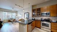 Located at 5455 Richmond Ave in Houston, TX, this well-appointed one-bedroom, one-bathroom residence offers a thoughtfully designed open-concept layout. Light wood-style flooring flows throughout, complementing the neutral color palette that lends a clean, modern aesthetic across all rooms.

The kitchen is a standout feature, showcasing warm wood cabinetry with glass-front uppers, dark granite countertops, a classic subway tile backsplash, and a full suite of stainless steel appliances including a refrigerator, range, microwave, and dishwasher. A peninsula with pendant lighting provides additional prep space and casual seating, connecting the kitchen seamlessly to the dining and living areas.

The living room is bright and welcoming, with large windows that allow generous natural light and views of the surrounding neighborhood. A ceiling fan adds comfort to the space.

The bedroom offers a comfortable retreat with a sizable window, hardwood-style flooring, and access to a generously sized walk-in closet with multi-level shelving and hanging rods. Two additional closets provide exceptional storage throughout the unit.

The bathroom features matching wood cabinetry, granite countertops, a full soaking tub with shower, and large-format tile flooring. A dedicated laundry area and a welcoming entrance complete this efficiently designed residence.