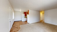 This single-floor residence offers a practical and functional layout across three bedrooms, one full bathroom, and a combined living, dining, and kitchen space. The open-concept living and dining area features neutral-toned carpet, textured ceilings, and large windows dressed with vertical blinds that allow natural light to fill the room. A front entry door with an adjacent window adds to the bright, airy feel of the main living space.

The kitchen is equipped with warm honey-toned wood cabinetry extending to the ceiling, offering generous storage. White appliances include a refrigerator, electric range with oven, and dishwasher. Wood-look vinyl flooring runs throughout the kitchen, providing durability and easy maintenance. A notable feature is the in-unit stacked washer and dryer, conveniently located within the kitchen area.

The three bedrooms are carpeted and finished with neutral walls, each offering wall-mounted heating units and windows for natural light. The primary bedroom provides a comfortable, well-proportioned space. Five closets throughout the unit ensure abundant storage options.

The full bathroom features wood-toned cabinetry with a single sink vanity, a large mirror, a combined tub and shower, and wood-look vinyl flooring, completing this well-organized and efficiently designed home.