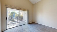 This thoughtfully laid-out 2-bedroom, 1-bathroom residence spans a single floor and makes excellent use of its space. The home is defined by striking vaulted ceilings that lend an open, airy feel throughout the main living areas, with soft carpet flooring underfoot and warm neutral tones on the walls creating a welcoming ambiance.

The spacious primary bedroom features soaring ceilings, plush carpeting, a large sliding glass door opening to a private balcony with outdoor views of surrounding trees, and convenient closet storage. The second bedroom is equally well-lit, with a generously sized window fitted with vertical blinds that allow natural light to filter in.

The kitchen is efficiently designed in a U-shaped layout, offering ample white cabinetry, granite-style countertops, white appliances including a gas range and dishwasher, and light wood-look vinyl flooring — all contributing to a clean, functional workspace. This same light vinyl flooring extends into the hallway and bathroom, providing a cohesive flow through the home.

The bathroom is practical and neatly finished, featuring vinyl plank flooring, a closet with a hanging rod for storage, and a vanity with mirror. Sliding closet doors are found in the bedrooms, maximizing usable space. A ceiling fan in the adjoining area adds to the home's comfort and functionality.