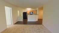 Located at 4730 W, this single-floor residence offers a practical and welcoming open-concept layout designed for comfortable everyday living. The kitchen is equipped with light wood cabinetry, black appliances including a full-size refrigerator and built-in microwave, and a peninsula-style breakfast bar with a dark countertop that serves as both a prep surface and casual dining space. The kitchen flows seamlessly into the main living area, creating an interconnected space ideal for entertaining or relaxing. The living area features rich, dark hardwood-style flooring that transitions into plush, light-toned carpeting, adding warmth and visual contrast throughout the space. The walls are finished in a soft, neutral cream tone that enhances the sense of brightness and openness. Trim details and white baseboards provide clean, classic accents throughout. A hallway visible from the main area hints at additional rooms beyond, while a door near the kitchen adds convenient access to utility or storage areas. The overall ambiance is clean, functional, and move-in ready, with a cohesive design that balances practicality with a comfortable residential feel.