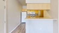 Located at 7701 W Fourth Ave in Kennewick, Washington, this one-bedroom, one-bathroom unit offers a efficiently designed floor plan that maximizes its compact footprint. The open-concept layout connects the kitchen and living area seamlessly, creating a sense of continuity throughout the main space. Hardwood-style flooring runs through the living area and kitchen, providing a clean, cohesive aesthetic, while the bedroom features plush carpeting for added comfort.

The kitchen is equipped with light wood cabinetry extending to the ceiling for ample storage, a white refrigerator, electric range, built-in microwave, and a stainless steel sink. A peninsula counter separates the kitchen from the living space, offering a practical surface for dining or food preparation.

The bedroom receives natural light through two windows with outdoor views of surrounding greenery. A built-in shelving and desk unit is integrated into one wall, adding functional storage and workspace. A ceiling fan provides additional airflow and comfort.

The bathroom features wood-look vinyl flooring, a tub-shower combination, a toilet, and a wood-toned vanity with sink. An adjacent closet with bi-fold doors provides convenient storage directly off the bathroom, keeping the overall layout organized and practical.