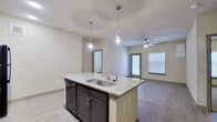This 2-bedroom, 2-bathroom single-story residence offers a thoughtfully designed open-concept layout with modern finishes throughout. The kitchen serves as the heart of the home, anchored by a large center island with a granite countertop, double sink, and stylish pendant lighting. Dark espresso cabinetry, a subway tile backsplash, black appliances, and light wood-style flooring complete the contemporary look. The kitchen flows seamlessly into the living room, which features a ceiling fan and a glass door alongside a large window that invites abundant natural light.

Both bedrooms are carpeted for comfort and include ceiling fans. The generously sized primary bedroom connects to a well-equipped en-suite bathroom featuring a dual-sink granite vanity, dark cabinetry, a tiled soaking tub with window, and a separate glass-enclosed shower. A spacious walk-in closet with built-in shelving and hanging rods provides ample storage. The second bathroom mirrors the same design aesthetic with a granite vanity and a tiled tub-shower combination. Throughout the residence, light wood-style flooring, neutral wall tones, and consistent dark cabinetry create a cohesive and modern living environment.