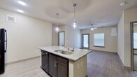 This 2-bedroom, 2-bathroom single-story residence offers a thoughtfully designed open-concept layout with modern finishes throughout. The kitchen serves as the heart of the home, anchored by a large center island with a granite countertop, double sink, and stylish pendant lighting. Dark espresso cabinetry, a subway tile backsplash, black appliances, and light wood-style flooring complete the contemporary look. The kitchen flows seamlessly into the living room, which features a ceiling fan and a glass door alongside a large window that invites abundant natural light.

Both bedrooms are carpeted for comfort and include ceiling fans. The generously sized primary bedroom connects to a well-equipped en-suite bathroom featuring a dual-sink granite vanity, dark cabinetry, a tiled soaking tub with window, and a separate glass-enclosed shower. A spacious walk-in closet with built-in shelving and hanging rods provides ample storage. The second bathroom mirrors the same design aesthetic with a granite vanity and a tiled tub-shower combination. Throughout the residence, light wood-style flooring, neutral wall tones, and consistent dark cabinetry create a cohesive and modern living environment.