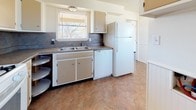 This single-floor residence offers a well-organized and functional layout designed for comfortable everyday living. The open living area serves as the heart of the home, featuring a combination of warm hardwood-style flooring and plush carpet, ceiling fans, and a sliding glass door that invites abundant natural light and outdoor views. The kitchen is fully equipped with white cabinetry, dark countertops, a gas range, dishwasher, refrigerator, and a double-basin sink beneath a window — all accented by a tile backsplash and tile flooring. A lazy Susan corner cabinet adds practical storage. The bedrooms are carpeted and bright, each benefiting from blinds-fitted windows that allow natural light to filter in. One bedroom features dual windows and a ceiling fan, while another includes a dedicated closet with a hanging rod, providing ample storage. The bathroom is clean and straightforward, outfitted with a full-size soaking tub with shower, toilet, vanity sink, and a window for ventilation. Throughout the home, a neutral color palette of whites and soft grays creates a bright, cohesive ambiance. The layout flows logically from the living and dining areas into the kitchen and private rooms, making the space practical and inviting.