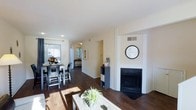 This two-story residence offers a thoughtfully designed interior that balances comfort and functionality. The main living area immediately draws attention with its rich, dark hardwood floors that extend seamlessly throughout the space, creating a warm and cohesive aesthetic. A built-in fireplace serves as a focal point in the living room, framed by clean white surroundings that enhance its visual impact.

The open-concept layout connects the living room to the dining area, which benefits from generous natural light streaming in through large windows. The dining space comfortably accommodates a full table and chairs, making it well-suited for both everyday meals and entertaining. A partial view into the kitchen reveals a functional pass-through layout that maintains the open feel of the main floor.

Recessed lighting supplements the natural light throughout, ensuring the space remains bright and welcoming at any time of day. Neutral, warm-toned walls provide a versatile backdrop that complements a variety of interior styles. The overall design is clean and contemporary, with practical details such as built-in storage and clearly defined living zones. Spanning two floors, this residence offers ample space for comfortable day-to-day living.