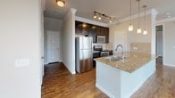 Located at 1316 Town Center Dr in Pflugerville, Texas, this single-story residence offers a well-designed open-concept layout that seamlessly connects the living, dining, and kitchen areas. Rich wood-style flooring flows consistently throughout the home, complemented by neutral-toned walls, crown molding, and crisp white baseboards that lend a clean, polished aesthetic.

The kitchen is a standout feature, equipped with dark espresso cabinetry, gleaming granite countertops, a tile backsplash, and a full suite of stainless steel appliances including a refrigerator, range, and microwave. A peninsula with a double basin sink and pendant lighting above serves as both a functional workspace and a casual dining spot, while track lighting illuminates the cooking area.

The bedrooms are generously proportioned, each finished with the same warm wood-style flooring and crown molding. Large windows with blinds allow ample natural light to fill each room while providing views of the surrounding neighborhood.

The bathroom is well-appointed with dark cabinetry, granite countertops, a large mirror, and a tiled tub-shower combination featuring a soaking tub. Wood-style flooring continues here, tying together the home's cohesive design. Overall, the space presents a comfortable and modern living environment suited for everyday living.