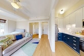 Located in the heart of Portland, OR, on SW Madison Street, this one-bedroom, one-bathroom residence offers a thoughtfully designed single-floor layout that makes efficient use of its intimate footprint. Light wood flooring flows throughout the unit, creating a warm and cohesive feel across every room.

The main living area connects seamlessly to both the bedroom and kitchen, offering an open, functional arrangement. A ceiling fan provides comfort overhead, while the living space benefits from natural light streaming in from large windows. The bedroom is generously proportioned relative to the overall unit size, featuring a tray ceiling detail and direct access to a private balcony framed by floor-to-ceiling French doors. These doors open to sweeping views of the Portland downtown skyline, filling the space with natural light and urban character. A classic radiator and an ornate gold-framed mirror add a touch of historic charm.

The kitchen stands out with a striking two-tone design: bold navy lower cabinetry contrasts with crisp white upper cabinets and subway tile backsplash. Stainless steel appliances, including a refrigerator, range, and over-the-range microwave, complete this efficient and stylish culinary space. A built-in open shelving unit adds additional storage.

The bathroom showcases classic tilework, with white subway wall tiles accented by teal border strips, penny-round mosaic floor tiles, and a frameless glass walk-in shower — a timeless aesthetic that reflects the building's heritage character.