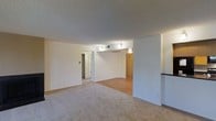 This single-floor residence offers a clean, open layout designed for comfortable everyday living. The main living area is finished with soft, neutral-toned carpeting that creates a warm and inviting atmosphere, while an adjoining section transitions to smooth hardwood flooring, providing a natural contrast that defines different functional zones within the space.

The ceilings throughout feature a classic textured finish, adding subtle visual interest overhead. Wall-mounted sconce lighting is positioned thoughtfully to illuminate the space with a soft, ambient glow, complementing the bright white walls that keep the interior feeling airy and open.

A partial wall acts as a natural divider, lending the layout a sense of structure without fully enclosing individual areas. This design choice promotes a connected, flowing feel between zones while still offering a degree of privacy and definition.

Storage is a practical highlight of this space, with what appears to be a dedicated closet area visible toward the rear, featuring sliding wood-toned doors — an efficient and stylish solution for organization. An additional doorway leads to a separate room or corridor, suggesting further utility space beyond the main living area.

Overall, the space presents a straightforward, functional design with neutral finishes throughout, making it highly adaptable for a variety of furnishing styles and personal tastes.