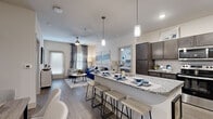This single-story, 2-bedroom, 2-bathroom home offers a thoughtfully designed open-concept layout that maximizes livability and flow. The combined kitchen and living area serves as the heart of the home, where a large granite-topped island with bar seating and stylish pendant lighting anchors the space. The kitchen is outfitted with dark espresso cabinetry, stainless steel appliances including a range, built-in microwave, and refrigerator, along with a classic white subway tile backsplash. Wood-style flooring runs throughout the main living areas, complementing the neutral, contemporary color palette. The living room is bright and inviting, featuring a ceiling fan, large windows dressed with decorative curtains, and access to the covered private patio. Both bedrooms are generously sized with plush carpet, ceiling fans, and large windows that allow ample natural light. The primary bedroom offers a comfortable retreat with dedicated closet space. Each bathroom features granite countertops, dark cabinetry vanities, and clean, modern fixtures, with the primary bath showcasing a tiled walk-in shower. Two closets provide practical storage throughout. The exterior features white lap siding, a covered concrete patio entry, and views of the surrounding landscaped grounds.