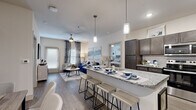 This single-story, 2-bedroom, 2-bathroom home offers a thoughtfully designed open-concept layout that maximizes livability and flow. The combined kitchen and living area serves as the heart of the home, where a large granite-topped island with bar seating and stylish pendant lighting anchors the space. The kitchen is outfitted with dark espresso cabinetry, stainless steel appliances including a range, built-in microwave, and refrigerator, along with a classic white subway tile backsplash. Wood-style flooring runs throughout the main living areas, complementing the neutral, contemporary color palette. The living room is bright and inviting, featuring a ceiling fan, large windows dressed with decorative curtains, and access to the covered private patio. Both bedrooms are generously sized with plush carpet, ceiling fans, and large windows that allow ample natural light. The primary bedroom offers a comfortable retreat with dedicated closet space. Each bathroom features granite countertops, dark cabinetry vanities, and clean, modern fixtures, with the primary bath showcasing a tiled walk-in shower. Two closets provide practical storage throughout. The exterior features white lap siding, a covered concrete patio entry, and views of the surrounding landscaped grounds.