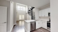 Located at 2430 Cheshire Bridge Rd NE in Atlanta, GA, this two-story residence offers a thoughtfully designed layout across two floors. The main level makes an immediate impression with soaring double-height ceilings and an abundance of natural light streaming through large transom-style windows. A striking black spiral staircase serves as the architectural centerpiece, connecting the two floors with both style and efficiency. The open kitchen is well-appointed with white shaker cabinetry, white quartz countertops, a subway tile backsplash, and a full suite of stainless steel GE appliances, including a refrigerator, range, over-the-range microwave, and dishwasher. French doors at the entrance add an elegant touch to the main living area. Wide-plank hardwood-style flooring runs consistently throughout both levels, creating a cohesive, modern aesthetic. Upstairs, the bedroom is a comfortable, well-proportioned retreat with a dedicated window overlooking greenery, a ceiling fan, and direct access to a spacious walk-in closet outfitted with wire shelving on multiple walls. The full bathroom features a white vanity with quartz countertop, a soaking tub/shower combination, and clean, neutral finishes. The overall ambiance is bright, clean, and contemporary.