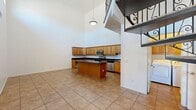 This two-story home offers a well-designed layout across two floors, with the main level comprising the majority of the living space. The entrance immediately impresses with soaring ceilings and large-format tile flooring that extends through the main living areas, anchored by a striking ornamental spiral staircase that serves as a true architectural centerpiece.

The expansive kitchen is a standout feature, offering abundant warm-toned wood cabinetry, dark granite countertops, a central island, and a full suite of stainless steel appliances including a range, microwave, dishwasher, and refrigerator. The kitchen benefits from the dramatic double-height ceiling above, lending an open, airy atmosphere.

The main level also includes two bedrooms with plush carpeting, a full bathroom finished with warm earth-tone tile, a dark granite vanity, a soaking tub, and a distinctive quatrefoil accent window. A dedicated laundry room with overhead cabinetry and side-by-side washer and dryer hookups adds everyday convenience.

The upper floor features a spacious open loft area with vaulted ceilings, plush carpet, a ceiling fan, and multiple windows that bring in ample natural light. The generously sized primary bedroom is also found on this level, offering a comfortable and private retreat. The home includes a closet and a second bathroom to complete the functional layout.