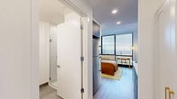 Located at 9 Homestead Place in Jersey City, NJ, this efficiently designed one-bedroom, one-bathroom unit offers a thoughtfully organized floor plan that maximizes every inch of space. The open layout seamlessly connects the kitchen and bedroom areas, creating a cohesive and functional living environment.

The kitchen is outfitted with modern stainless steel appliances, including a refrigerator, built-in microwave, and dishwasher, complemented by a sleek electric cooktop. White subway tile backsplash, clean white countertops, and dark wood cabinetry give the kitchen a contemporary and polished aesthetic.

The bedroom is the heart of the unit, featuring light wood-style flooring, crisp white walls, and large floor-to-ceiling windows that flood the space with natural light and frame impressive elevated views of the Jersey City and New York City skyline. Recessed lighting and a neutral color palette enhance the airy, modern feel of the room.

The bathroom is clean and minimal, featuring large-format tile flooring, a glass-enclosed walk-in shower with white subway tile surround, a dark wood vanity with a white countertop, and straightforward modern fixtures throughout.

Overall, this unit delivers a streamlined, contemporary design with high-quality finishes and standout city views, making it an efficient and stylish urban living space.