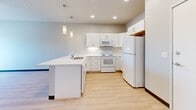 This one-bedroom, one-bathroom unit in Sheboygan, Wisconsin offers a thoughtfully designed single-floor layout that maximizes its compact footprint. Light wood-tone flooring flows throughout the main living areas and bedroom, lending a cohesive, clean aesthetic to the space.

The kitchen serves as a focal point of the unit, featuring an open-concept design anchored by a peninsula with a white countertop that provides both workspace and a casual dining option. White cabinetry lines the walls with ample storage, complemented by a full suite of appliances including a refrigerator, electric range, microwave, and sink. Pendant lights hang above the peninsula, while recessed lighting illuminates the wider area. The elevated ceiling height in this zone adds an airy sense of volume.

The bedroom is a well-proportioned private retreat, featuring a window that admits natural light and offers a view of the surrounding neighborhood. Light-toned walls and wood flooring continue here, and the room connects to a dedicated closet for storage convenience.

The bathroom is finished with large-format tile flooring, a walk-in shower with a clean white surround, a vanity with white cabinetry and integrated sink, and a framed mirror. The neutral palette and simple fixtures create a functional, tidy space throughout.