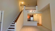Located at 890 S Matlack Street in West Chester, Pennsylvania, this two-story residence offers an impressive and functional layout designed for comfortable living. The main level immediately draws the eye upward with soaring double-height ceilings that lend a sense of openness and grandeur to the living area. Neutral-toned carpeting and crisp white walls create a clean, versatile backdrop throughout the space.

The kitchen is positioned as a central focal point on the main floor, featuring warm wood-toned cabinetry, stainless steel appliances including a full-size refrigerator, and a peninsula-style counter that opens to the living area — ideal for casual dining or entertaining. Track lighting illuminates the kitchen efficiently, while flush-mount fixtures provide consistent ambient light throughout.

A staircase with dark wood treads and a white spindle railing leads to the upper level, where an open loft-style overlook gazes down into the living space below, enhancing the home's airy, connected feel. The upper floor provides additional living or sleeping quarters, taking full advantage of the vertical space the two-story design affords. The overall ambiance is bright, modern, and welcoming, making this West Chester property a well-appointed and thoughtfully designed residence.