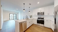 Located in Merriam, Kansas, this thoughtfully designed one-bedroom, one-bathroom unit offers a clean, modern aesthetic throughout its efficiently organized single-floor layout. Warm hardwood-style flooring flows seamlessly across every room, creating a cohesive and inviting atmosphere.

The kitchen serves as a centerpiece of the open-concept living area, featuring crisp white shaker cabinetry, light quartz countertops, and a full suite of stainless steel appliances including a refrigerator, electric range, built-in microwave, and dishwasher. A peninsula with seating accommodates multiple bar stools and is accented by sleek pendant lighting with matte black fixtures, tying into the consistent modern hardware found throughout.

The living room is bright and open, bathed in natural light from a large sliding glass door that leads directly to a private balcony, offering outdoor views of the surrounding area. The bedroom is a comfortable, well-proportioned space with a dedicated window that brings in additional natural light, complemented by a ceiling fan and a dedicated closet.

The bathroom is finished in a clean, contemporary style with white tile, a glass-enclosed shower, white vanity, and matte black hardware accents. A dedicated laundry room with full-size washer and dryer hookups completes this well-appointed home.