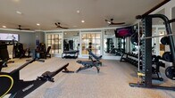 Located at 301 Newbrook Dr in Charleston, SC, this fitness center offers a thoughtfully designed, single-floor workout facility that caters to a wide range of exercise needs. The space is finished with durable speckled flooring and features elegant crown molding, recessed lighting, and multiple ceiling fans that maintain a comfortable atmosphere throughout.

The cardio zone is lined along large windows that invite abundant natural light and outdoor views of the surrounding landscape, housing a row of treadmills, elliptical machines, rowing machines, and stationary cycling bikes — many equipped with individual display screens. Strength training is equally well represented, with a full rack of dumbbells in varying weights, multiple Technogym selectorized machines targeting major muscle groups, a power rack with a barbell station, and adjustable benches for free weight exercises.

Full-length mirrors are strategically placed throughout, expanding the sense of space and allowing for form checks during workouts. Wall-mounted televisions provide entertainment options across the facility. Steel-framed glass interior windows and doors add an architectural refinement to the space while allowing light to flow freely between areas. The overall ambiance is clean, modern, and inviting, making this fitness center a standout amenity for the Charleston community it serves.
