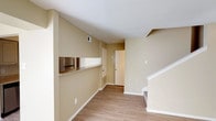This two-floor residence offers a well-organized layout across both levels, finished throughout in warm neutral tones with light wood-style flooring on the main floor and plush carpet in the upper-level rooms. The main level features an open living and dining area highlighted by a classic fireplace with a white mantel, a ceiling fan with light fixture, and a sliding glass door that fills the space with natural light. A pass-through counter with a granite-style surface connects the living area to the galley-style kitchen, which is equipped with white cabinetry, laminate countertops, a double stainless steel sink, electric range, and a full-size refrigerator. A staircase leads to the upper level, where the bedrooms are carpeted and include ceiling fans and windows for natural ventilation. The primary bedroom features a private en-suite bathroom and access to a generously sized walk-in closet with dual clothing rods and a window. The bathrooms include a tub-shower combo with white tile surround and a separate bathroom with a glass-enclosed shower. Practical touches such as HVAC vents, towel bars, and ample storage space are found throughout, making this a functional and comfortable multi-level home.