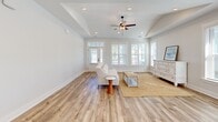 Located at 6146 Liberty Hall Dr in Leland, NC, this well-appointed single-story home offers three bedrooms and three bathrooms within a thoughtfully designed floor plan. The open-concept kitchen and living area serves as the heart of the home, featuring gray shaker-style cabinetry, granite countertops with a central island, a white tile backsplash, stainless steel appliances including a wall oven, and a sleek range hood. Light hardwood-style flooring flows throughout the main living areas, complemented by vaulted ceilings and large windows that bathe the space in natural light. The living room provides a bright, airy atmosphere with direct access to the front entry. Each bedroom is carpeted and includes ceiling fans and generous windows with views of the surrounding neighborhood. The spacious primary bedroom features a tray ceiling for added architectural interest. The three bathrooms include clean, modern finishes, with one showcasing soft blue cabinetry and light wood-look flooring. A dedicated laundry room offers side-by-side washer and dryer with wire shelving above. The attached garage provides additional utility space. Outside, the home is framed by tidy landscaping along a well-maintained street in a welcoming neighborhood community.