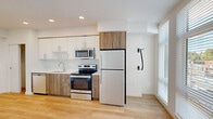 Located in the heart of Portland's vibrant West End neighborhood, this modern studio unit at 1670 SW Alder St offers a well-designed, efficient layout that makes excellent use of its compact footprint. The open-plan living area is anchored by light hardwood flooring that flows seamlessly throughout the entire space, contributing to a bright and cohesive aesthetic.

The kitchen is a standout feature, outfitted with a full suite of stainless steel appliances including a refrigerator, electric range, microwave, and dishwasher. Cabinetry combines crisp white upper cabinets with warm wood-toned lower cabinets, paired with clean white countertops and a stainless steel sink — creating a contemporary, functional workspace.

The living area benefits from large floor-to-ceiling windows that flood the space with natural light and offer views of the surrounding urban streetscape. The clean white walls and recessed lighting reinforce the unit's modern, minimalist character.

The bathroom is thoughtfully appointed with warm wood cabinetry, a white countertop vanity with an undermount sink, a large mirror, and hardwood-style flooring. A stacked washer and dryer unit is conveniently integrated within the bathroom, adding practical in-unit laundry to the space's amenities.